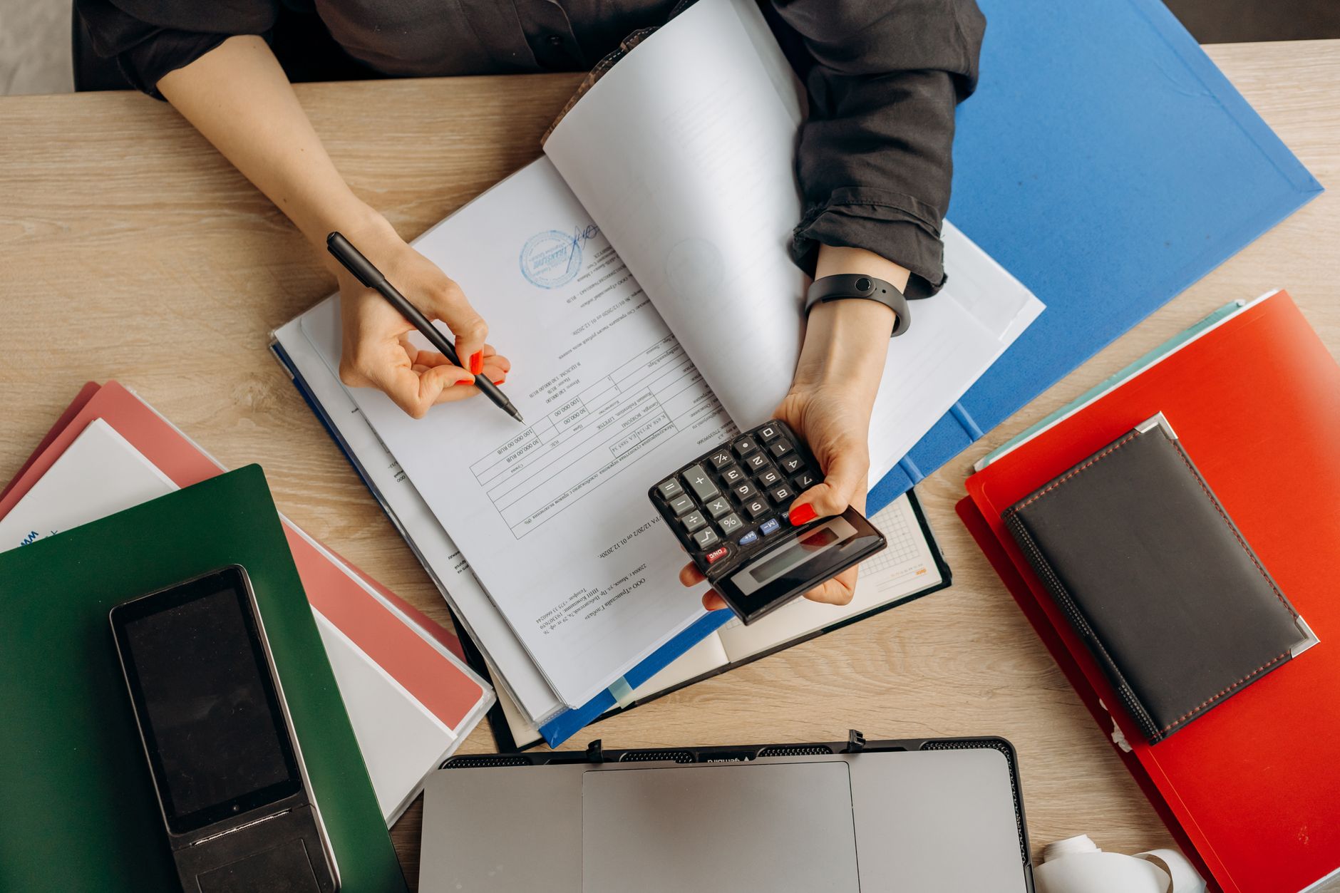 a person reviewing invoices on a computer with paperwork and calculator on a desk