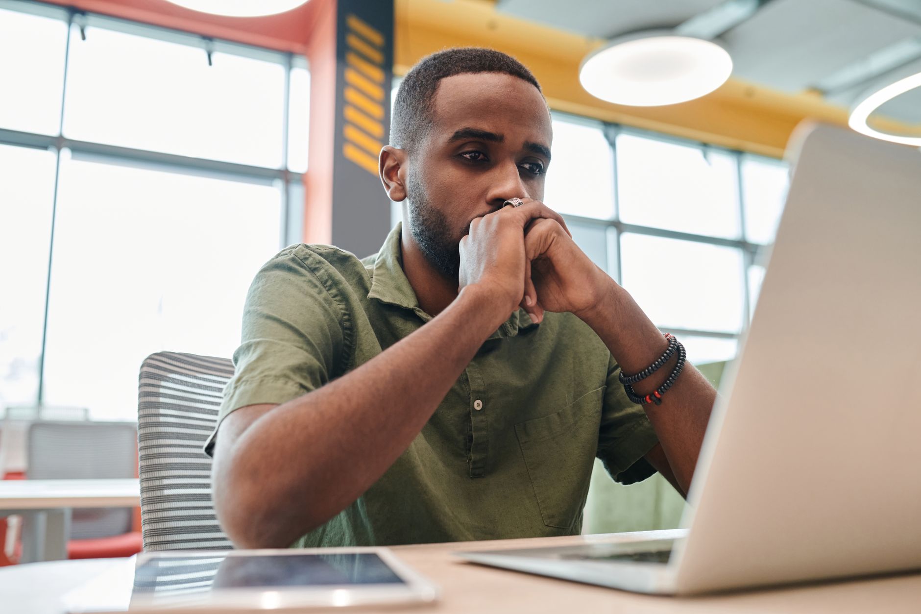 A person sits at a desk in a modern office, looking thoughtfully at a computer screen showing an AI assistant interface.