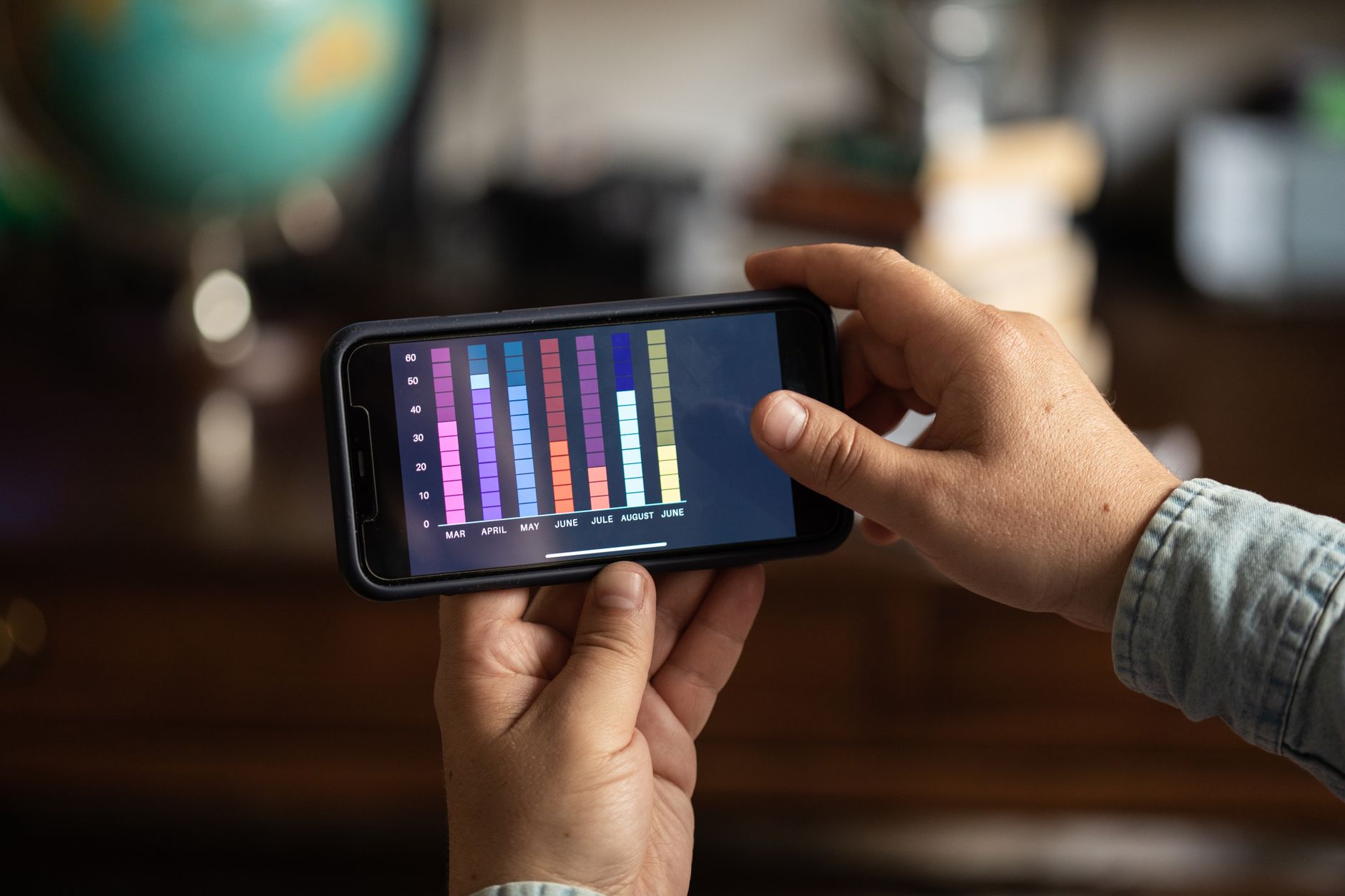 A person holds a smartphone showing colorful data charts while sitting at a desk.