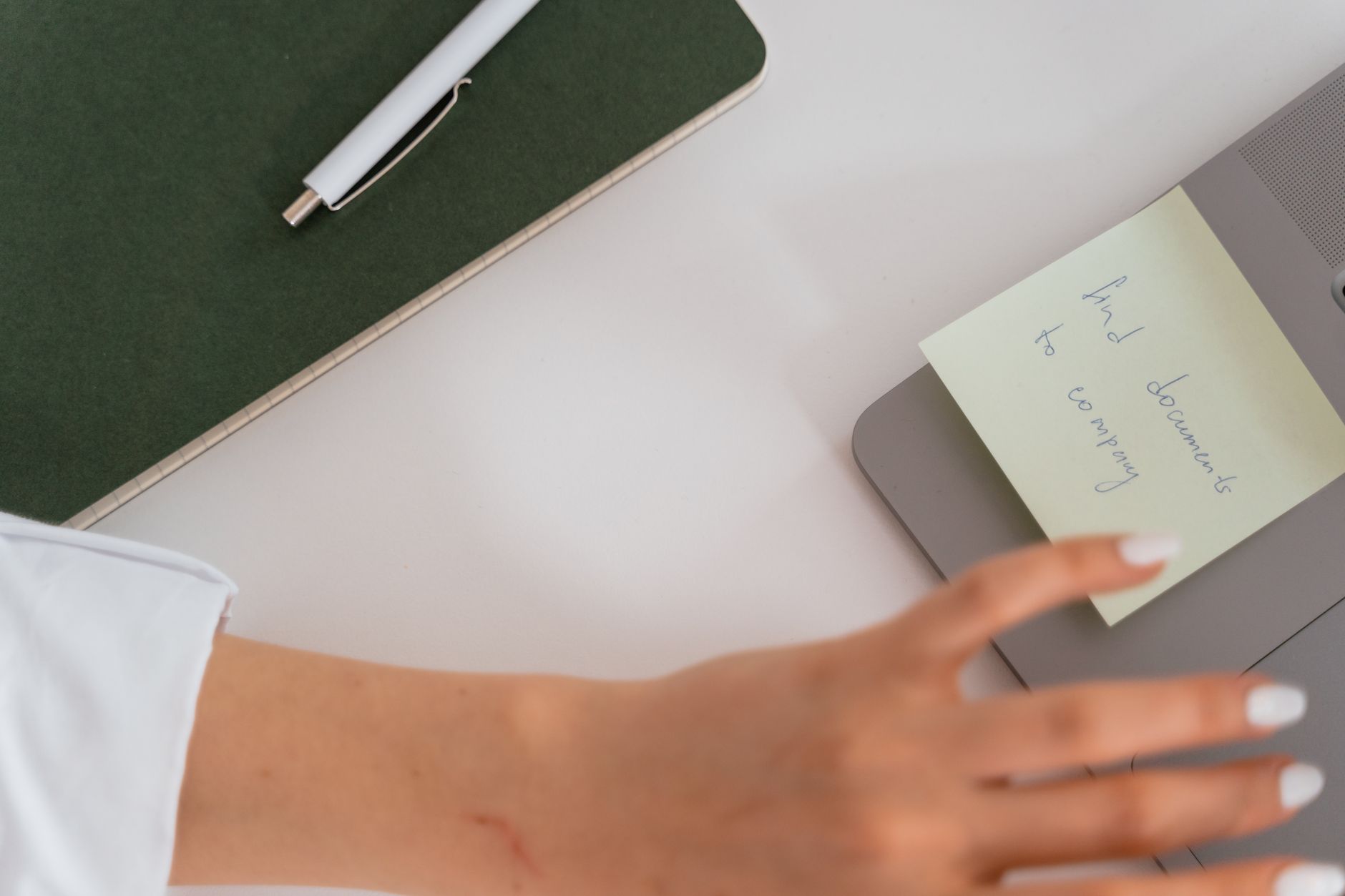 A white robotic hand reaches toward a laptop keyboard on a clean desk.