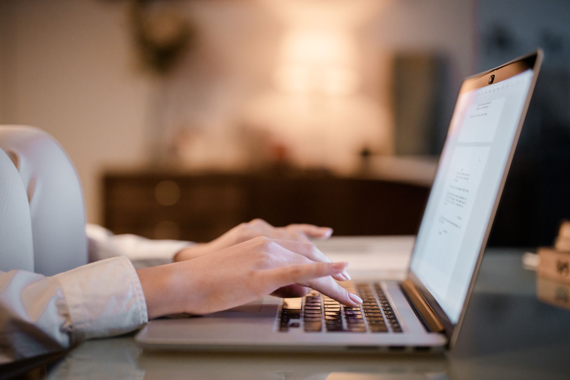 A person typing a question into an AI tool on a laptop at a home desk with soft natural light.