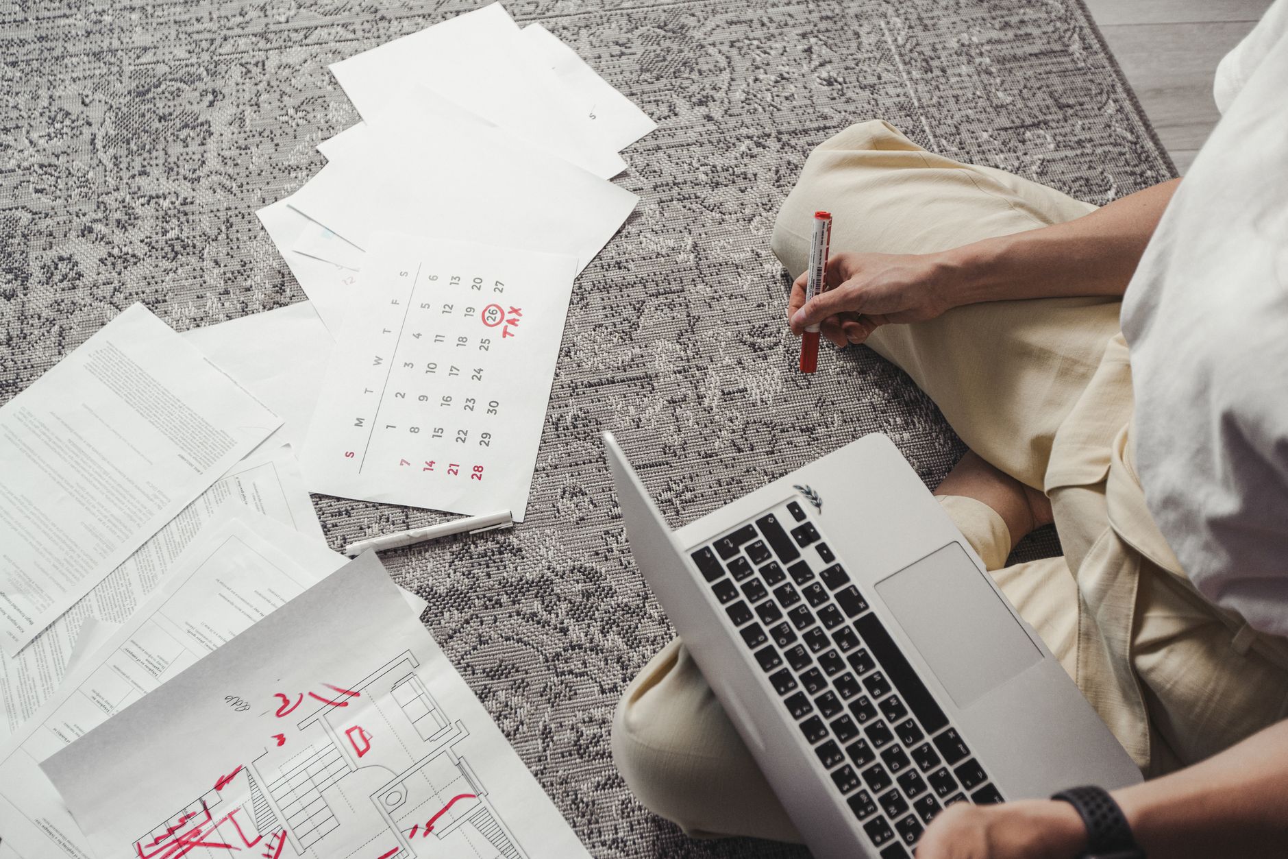 A person at a bright desk uses a laptop that shows a travel itinerary, a calendar, and a map while holding a smartphone.