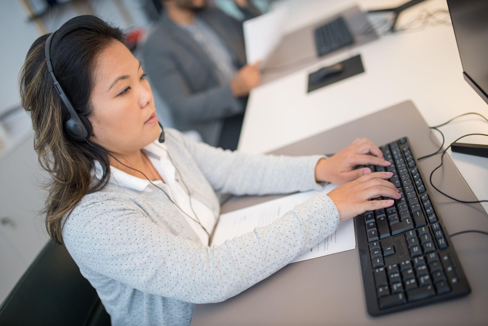 A person wearing a headset typing on a computer in a busy customer service office